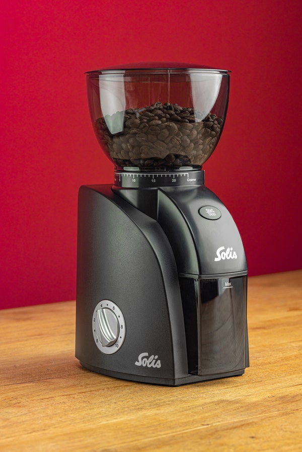 Solis Scala Zero Static Kaffeemühle auf Holztisch vor rotem Hintergrund, gefüllt mit Kaffeebohnen